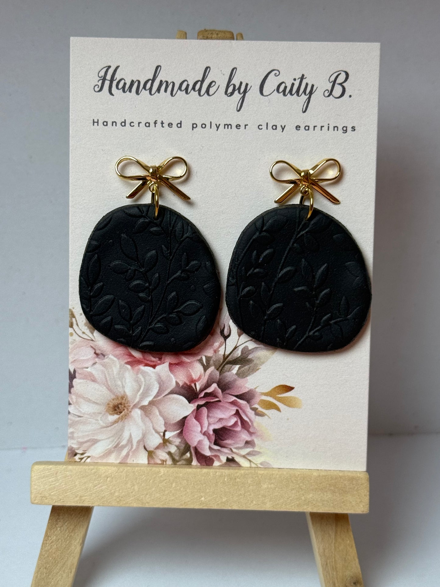 black floral textured earrings with gold bow tops